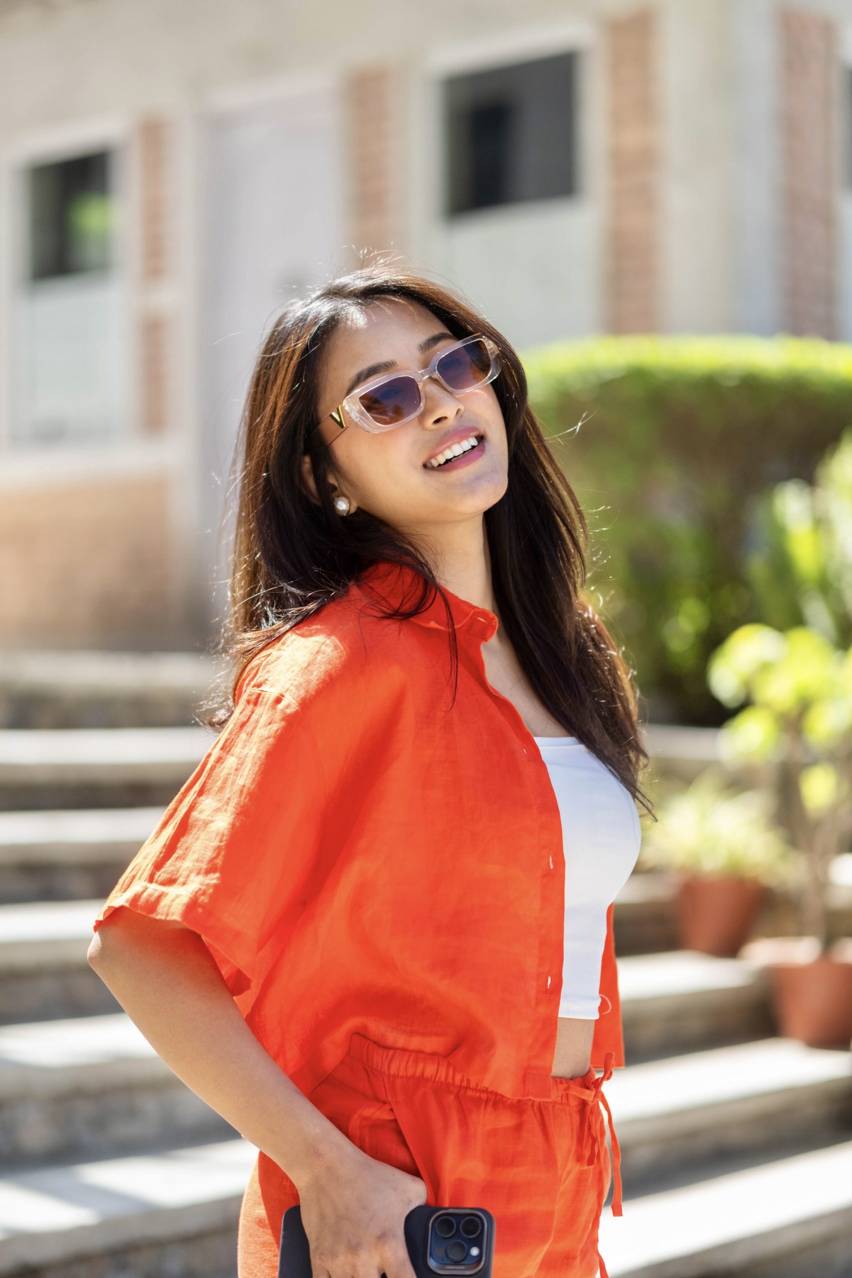 Roshani Shrestha with orange dress form humtto, makeup and black sunglasses standing at stairs
